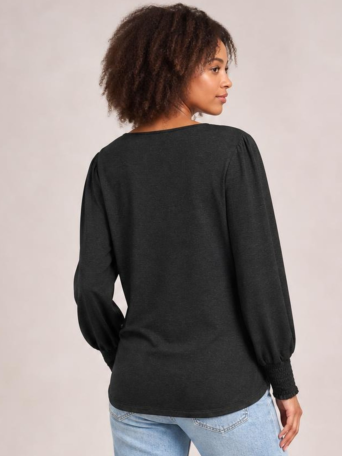 Back view of a model wearing a black lantern sleeve T-shirt with voluminous long sleeves, ribbed cuffs, and a relaxed, curved hem silhouette.