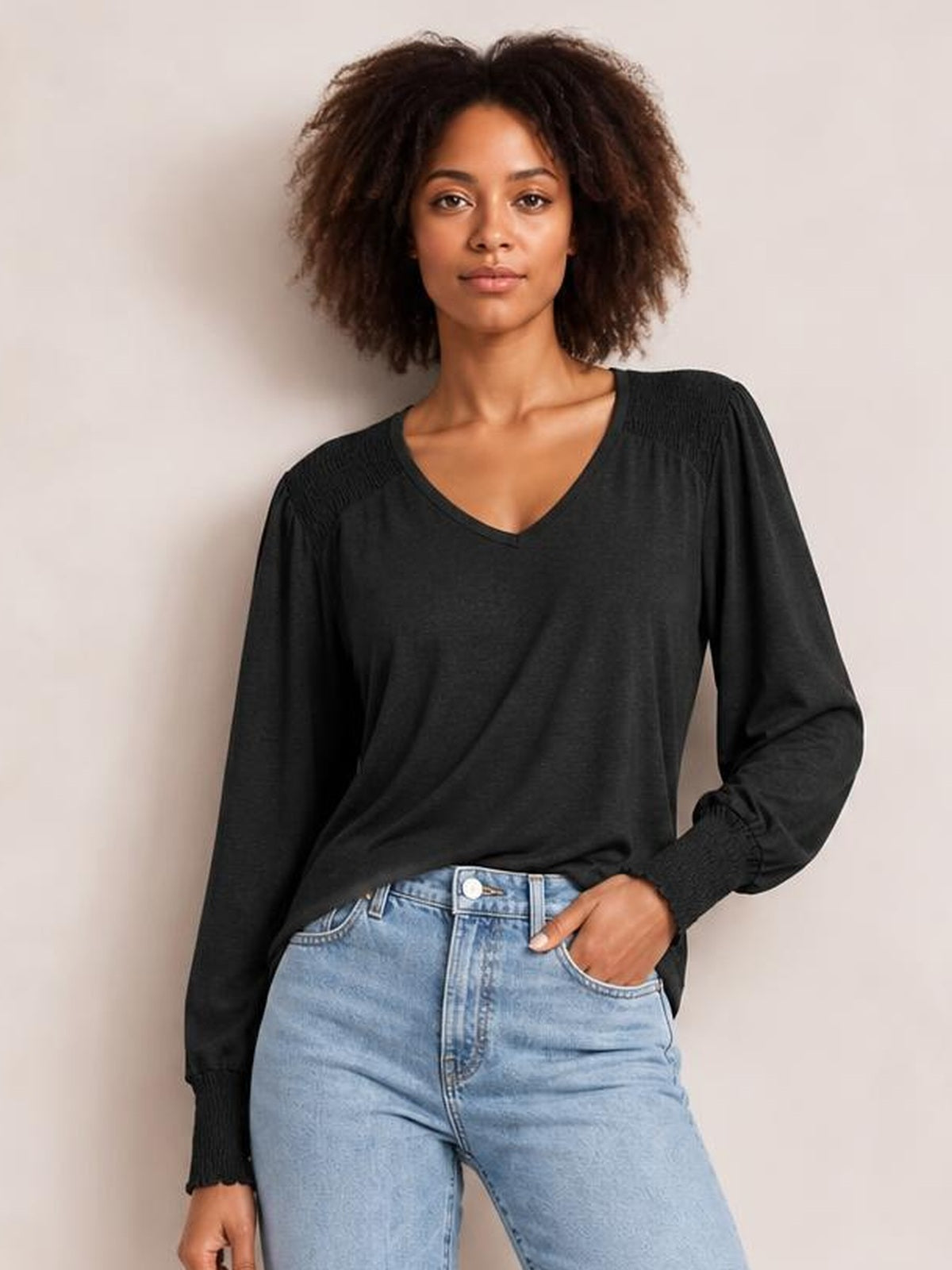 Model wears a black V-neck lantern sleeve T-shirt with a relaxed silhouette, gathered shoulder details, and elastic cuffs, posing with one hand in her jeans pocket.