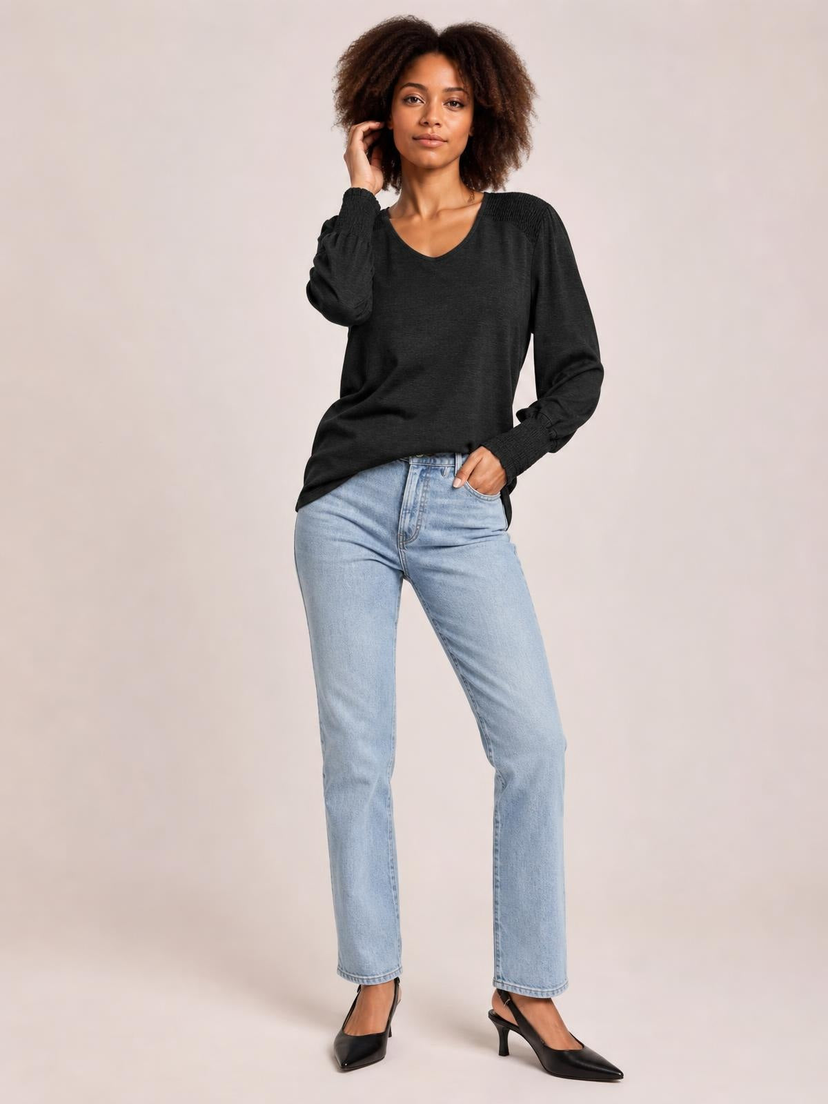 Model wearing a black V-neck lantern sleeve T-shirt with a relaxed silhouette, gathered cuffs, and slight drape, posing with one hand in her jeans pocket.