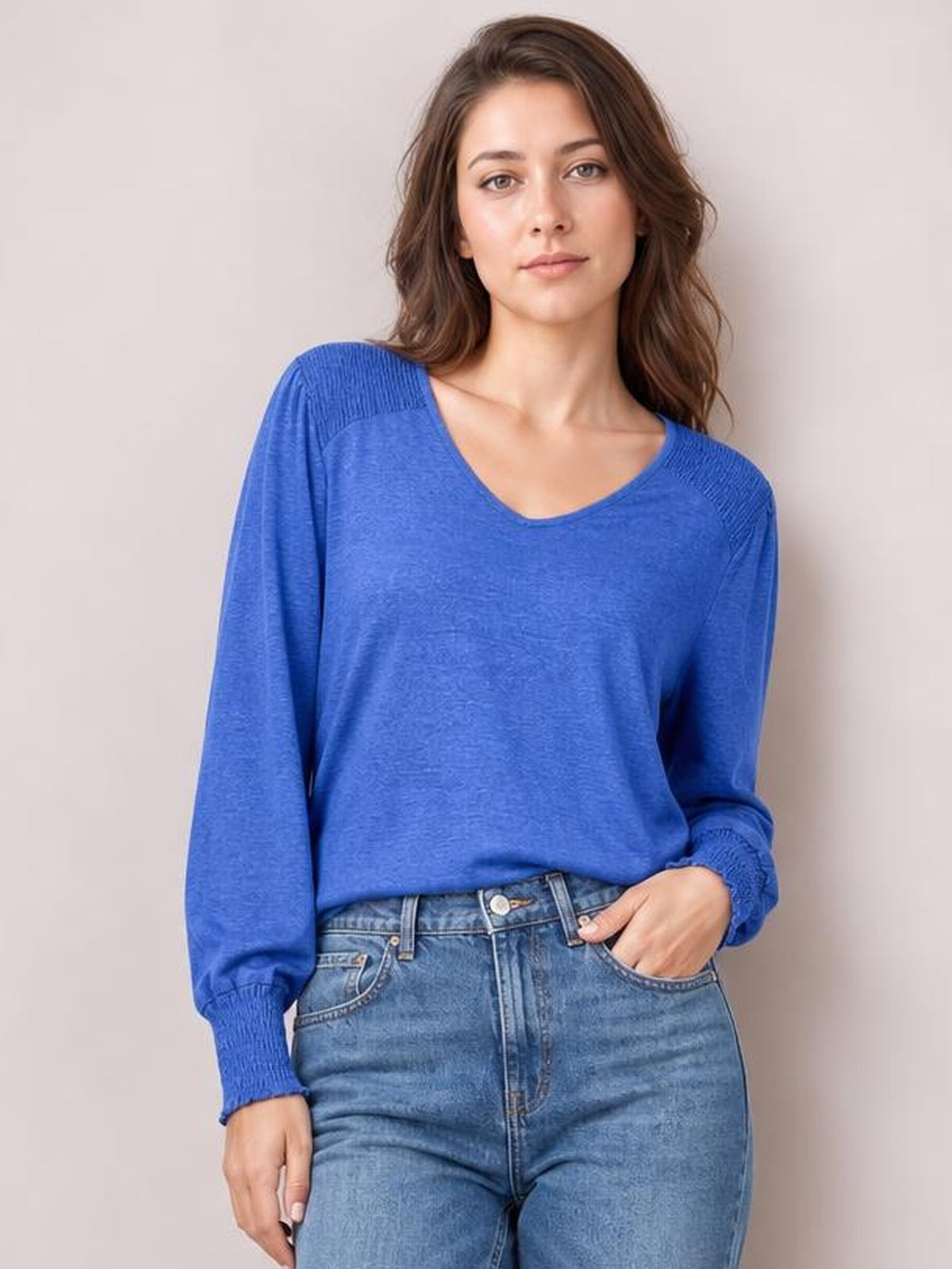 Model poses with one hand in her jeans pocket wearing a royal blue V-neck lantern sleeve T-shirt with gathered cuffs and a relaxed silhouette.