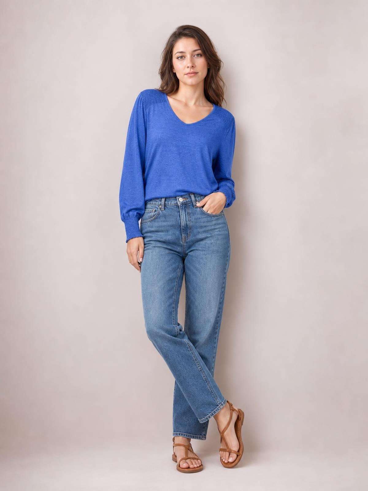 A model poses with one hand in her jeans pocket, wearing a cobalt blue V-neck T-shirt with relaxed lantern sleeves, gathered cuffs, and a fluid silhouette.