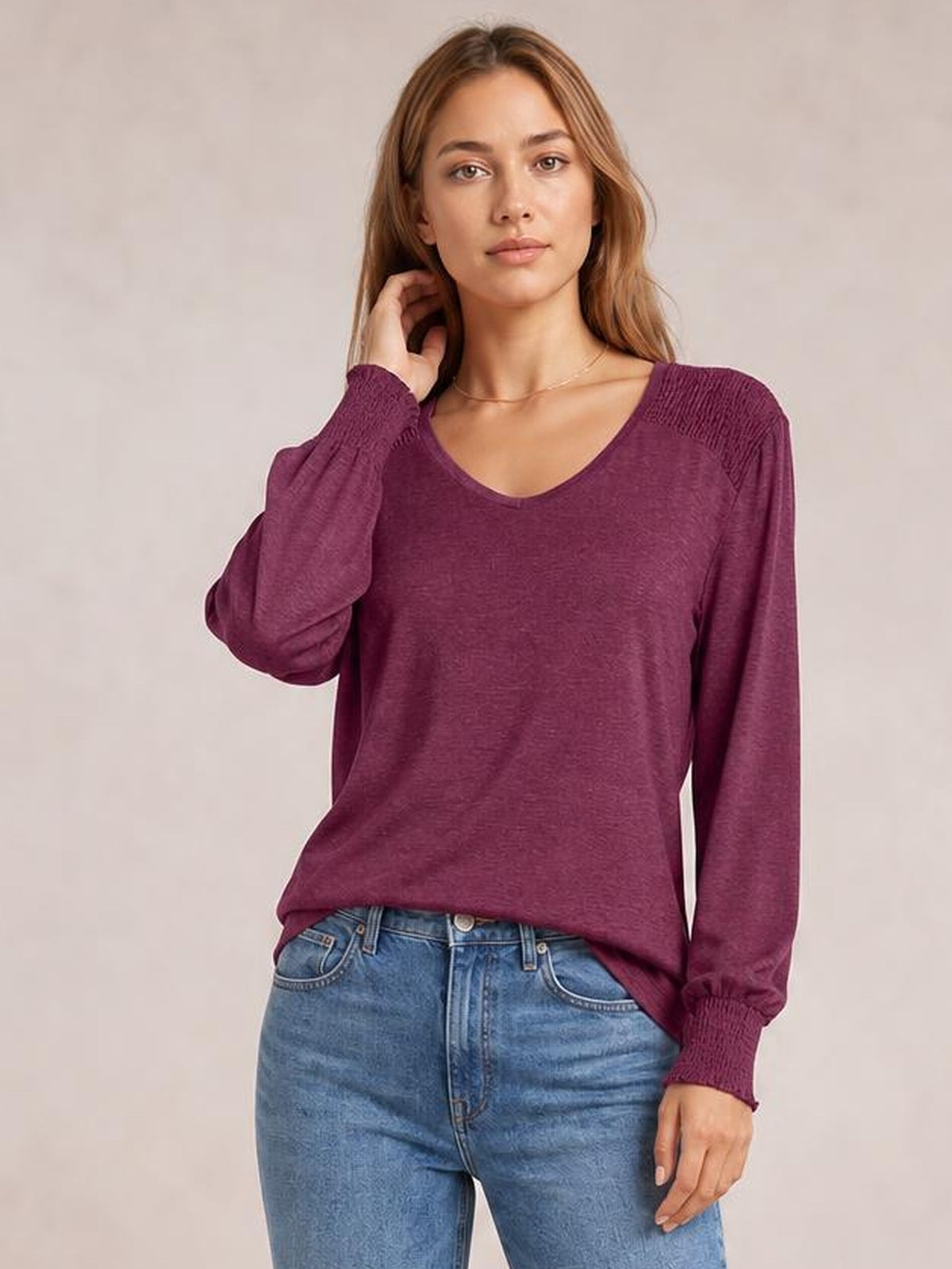 Model wearing a burgundy V-neck lantern sleeve T-shirt with a relaxed silhouette, gathered cuffs, and long sleeves, posing with one hand near her hair.