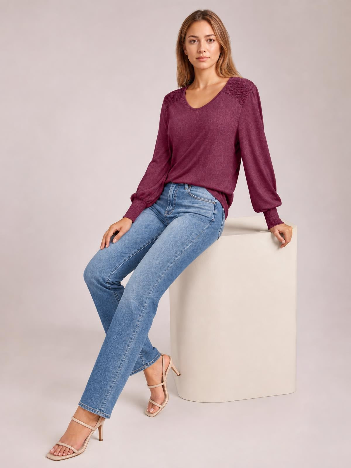 Model seated in a burgundy V-neck T-shirt with long lantern sleeves, gathered cuffs, shoulder detailing, and a relaxed silhouette.
