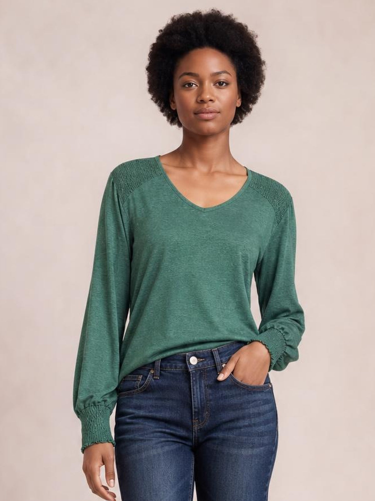 A model wears a green V-neck T-shirt with voluminous lantern sleeves, gathered cuffs and shoulder detailing, posed front-facing with one hand in a jeans pocket.