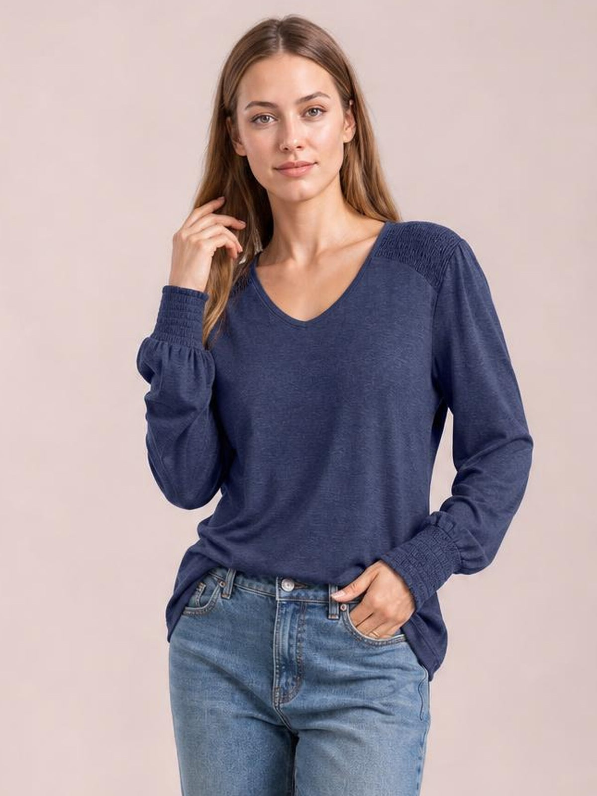 A model poses in a navy V-neck T-shirt with long lantern sleeves, gathered cuffs, and a relaxed silhouette, one hand resting in her jeans pocket.