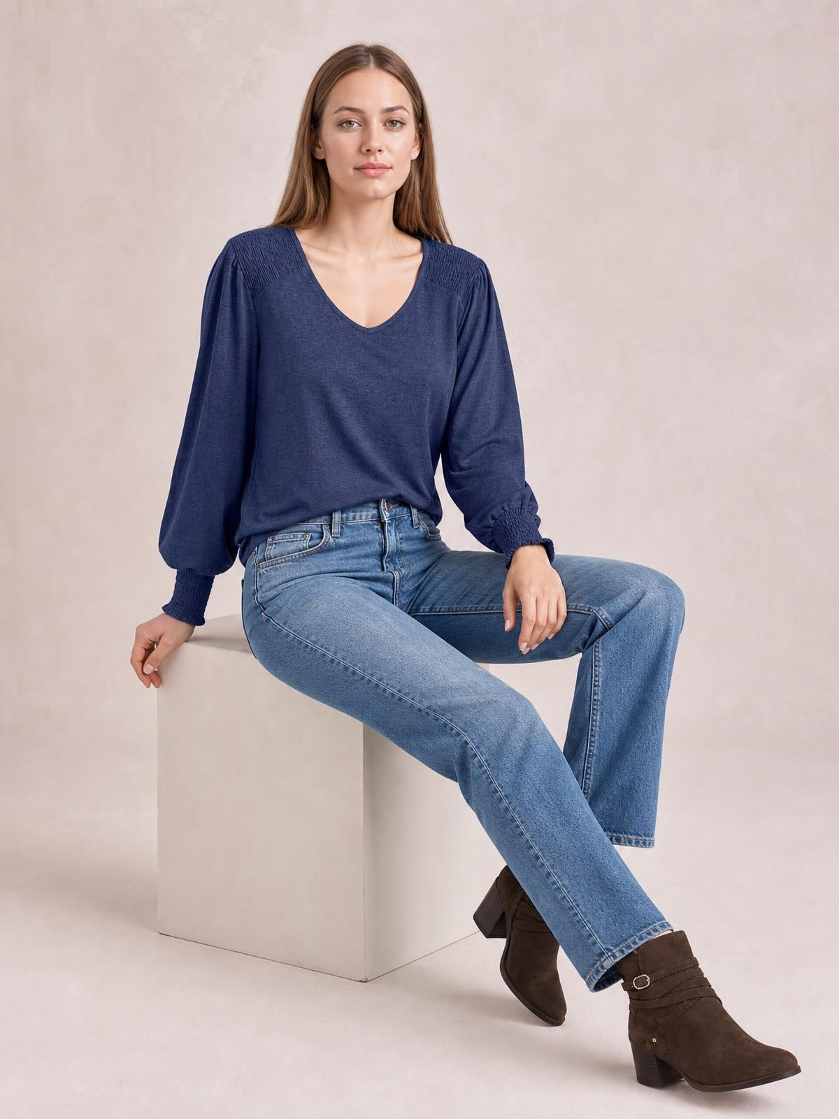A seated model wears a navy V-neck T-shirt with voluminous lantern sleeves, gathered shoulder panels, and elasticized cuffs for a relaxed silhouette.