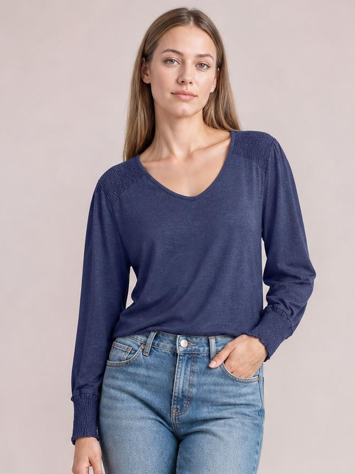 Model wearing a navy V-neck lantern sleeve T-shirt with a relaxed silhouette, gathered shoulder details, and gathered cuffs, posing with one hand in her jeans pocket.