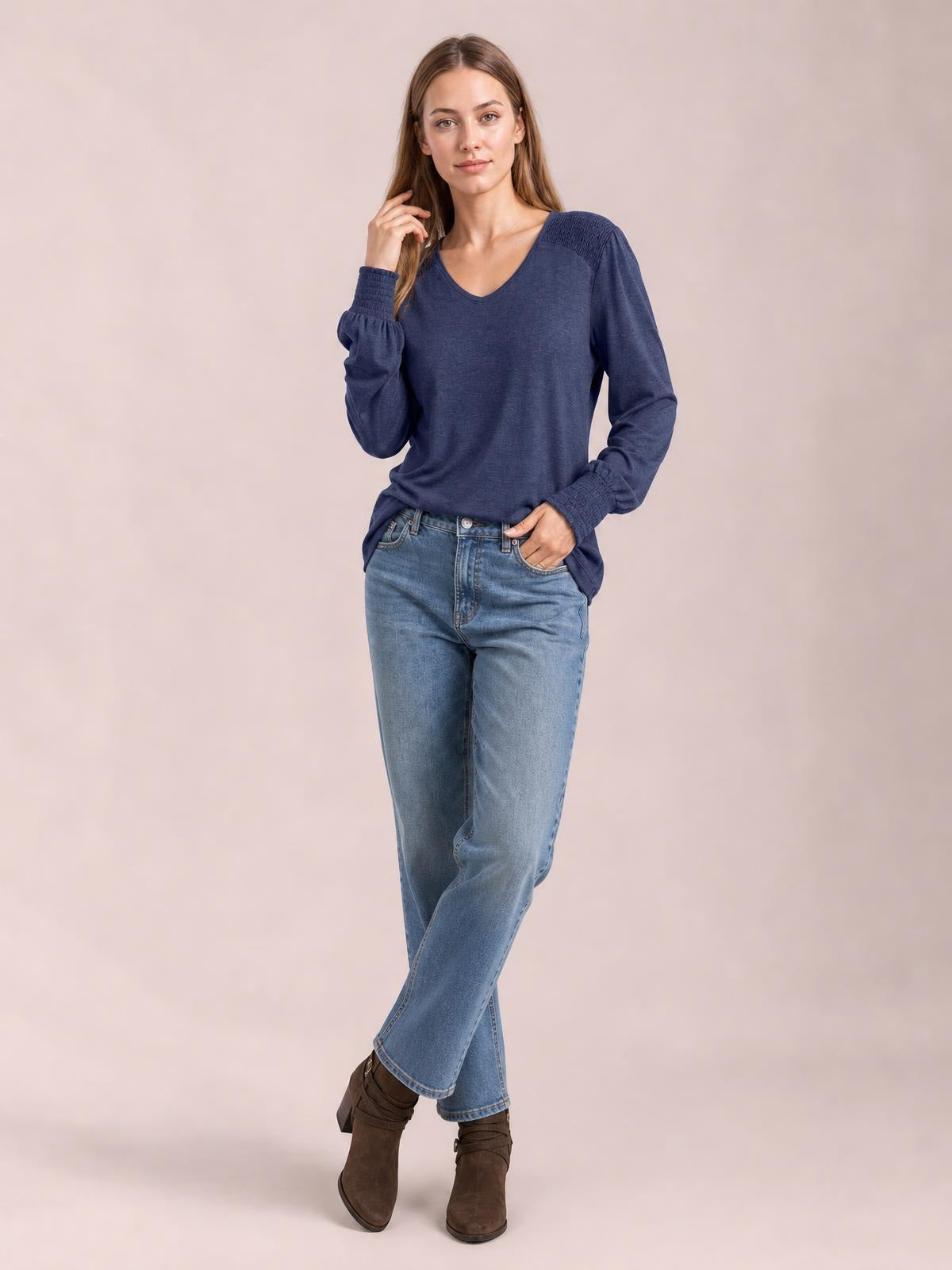 A model poses in a navy V-neck T-shirt with long lantern sleeves, gathered cuffs, and a relaxed silhouette, one hand touching her hair and the other in her pocket.