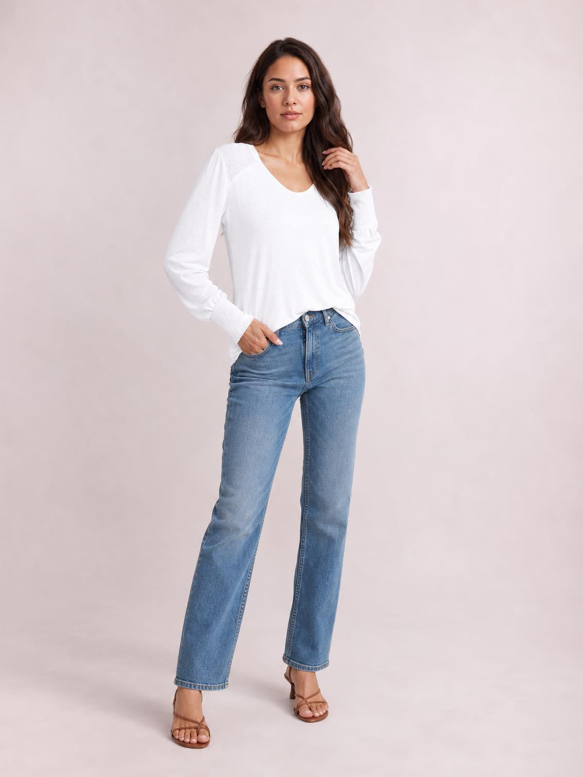 Model poses in a white V-neck T-shirt with gently gathered lantern sleeves, a relaxed silhouette, and long cuffs, paired with jeans.