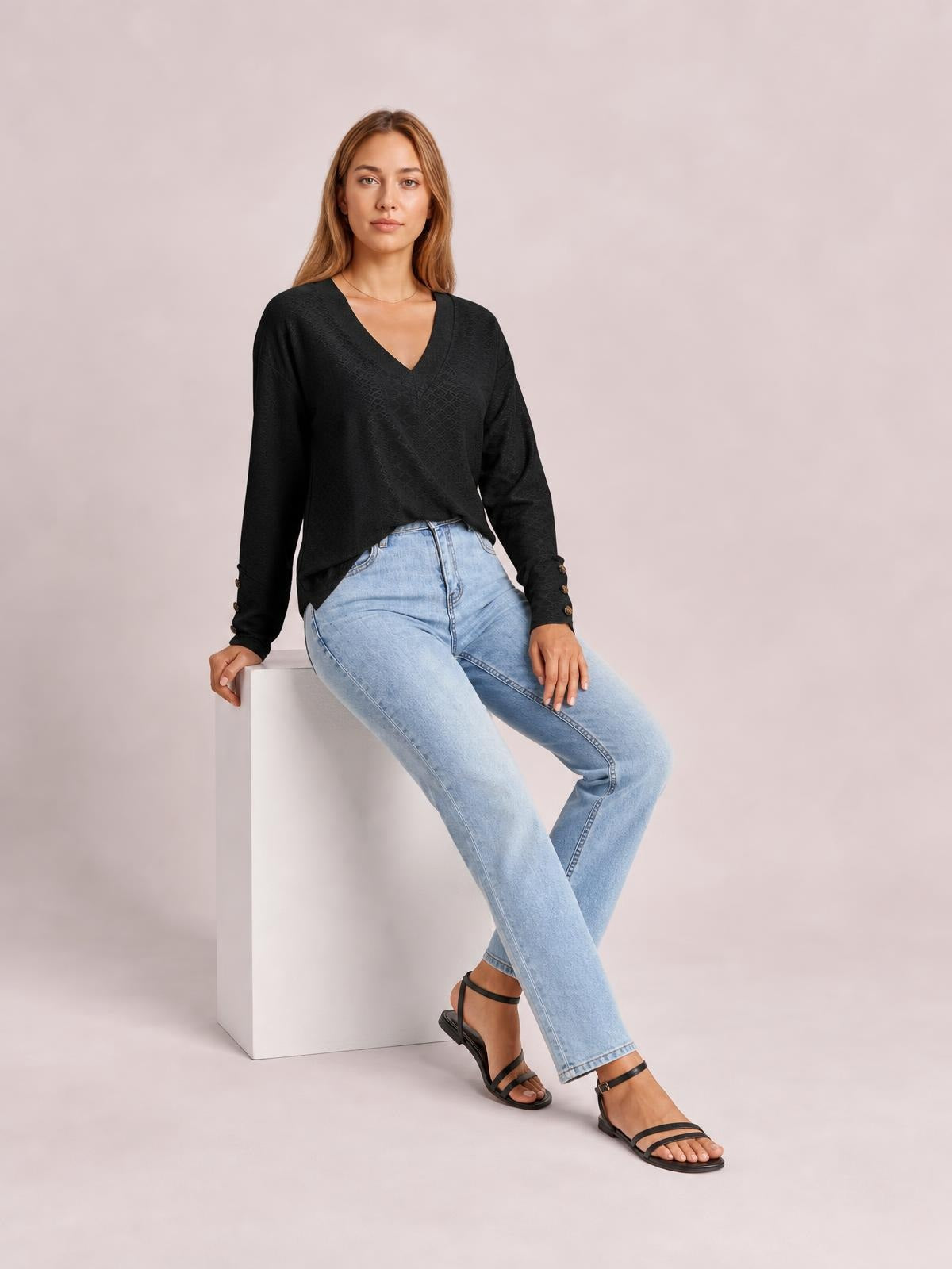 A model sits in a black V-neck long sleeve blouse with a relaxed regular silhouette, softly draped hem, and buttoned cuffs.