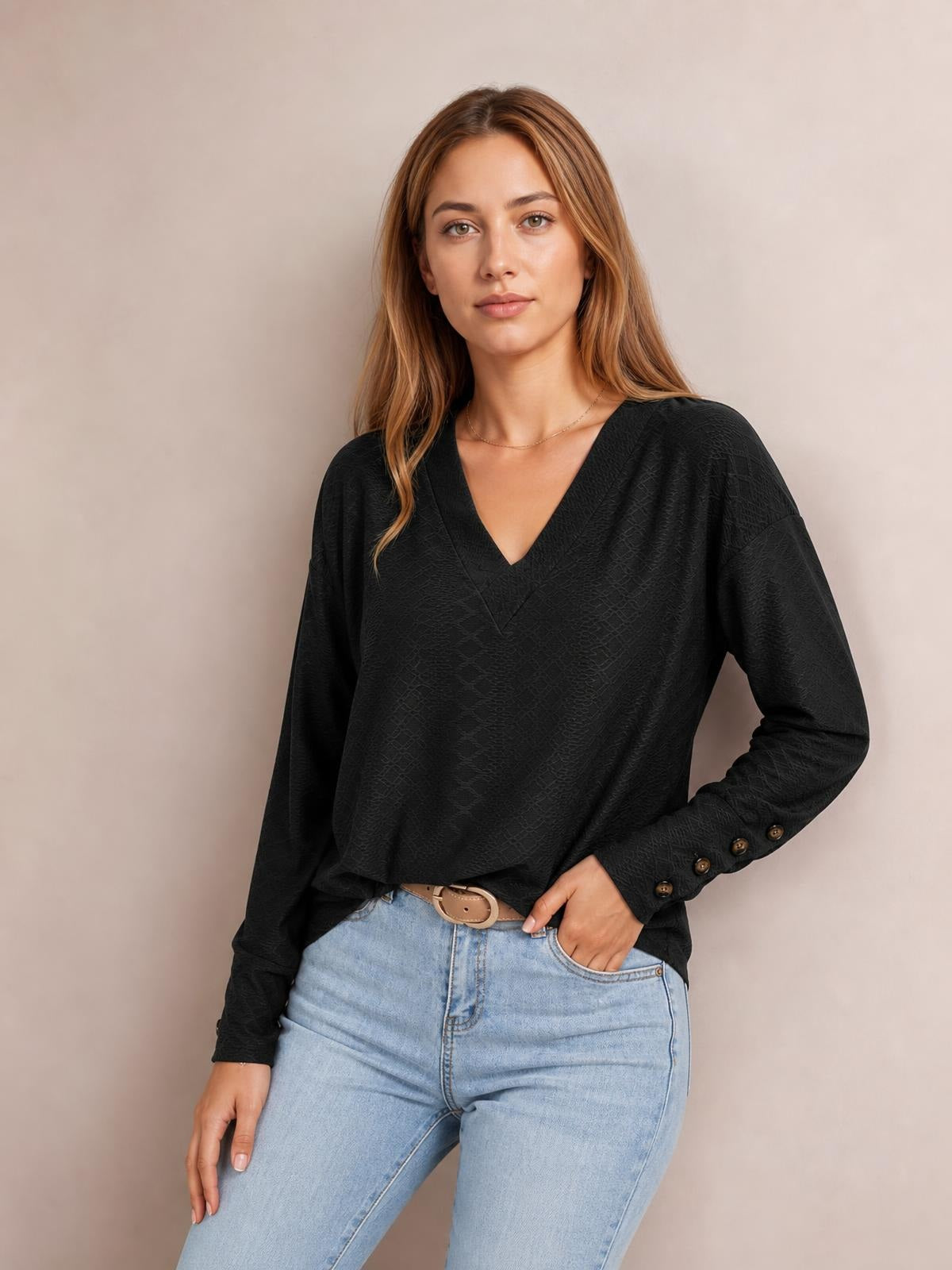 Model wears a solid black V-neck long sleeve blouse with a relaxed regular silhouette, buttoned cuffs, and one hand resting in her jeans pocket.