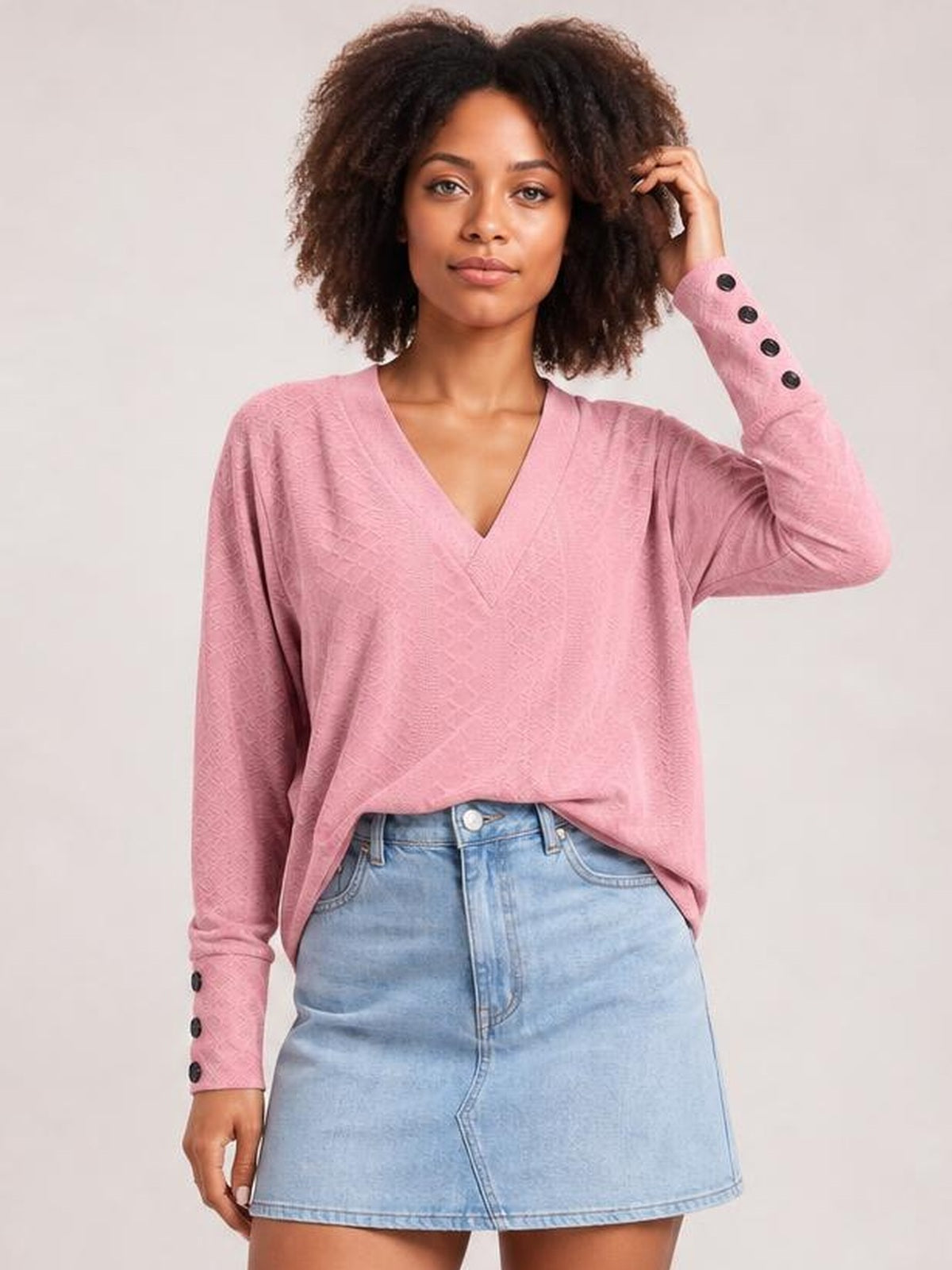 A model wears a pink solid V-neck long-sleeve blouse with a relaxed regular silhouette and buttoned cuffs, posing with one hand in her hair.