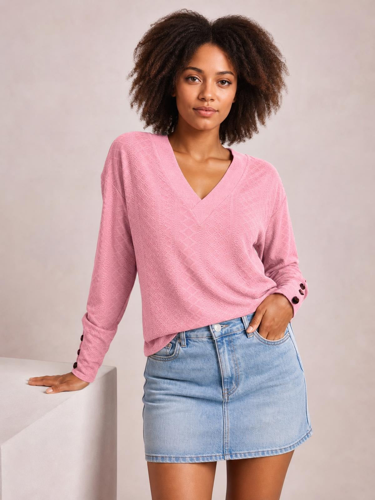 Model wearing a pink V-neck long sleeve blouse with a relaxed regular silhouette, subtle textured pattern, and buttoned cuffs, posed with one hand in her pocket.
