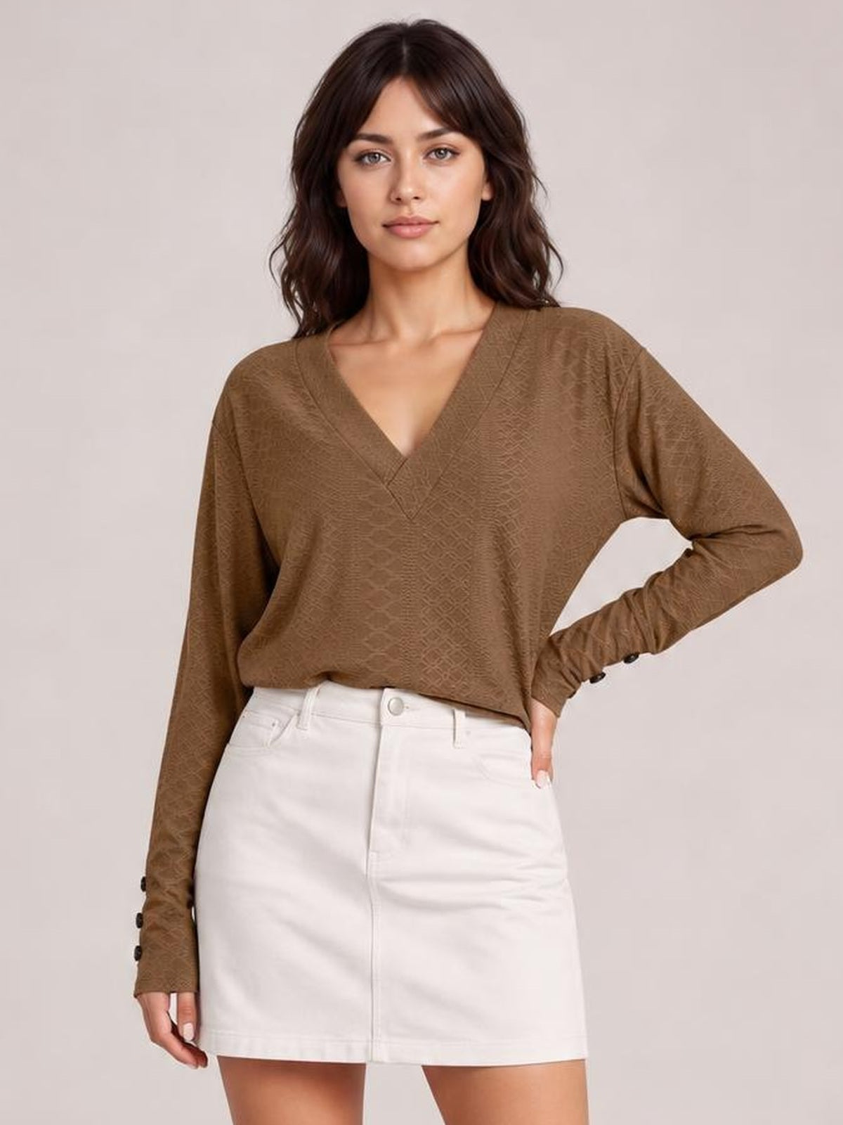 Model wearing a brown V-neck long sleeve blouse with a relaxed regular silhouette, subtle textured finish, and buttoned cuffs, posing with one hand on her hip.