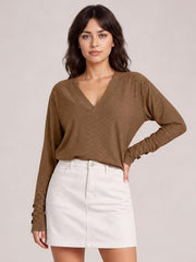 Model wearing a brown V-neck long sleeve blouse with a relaxed regular silhouette, subtle textured finish, and buttoned cuffs, posing with one hand on her hip.