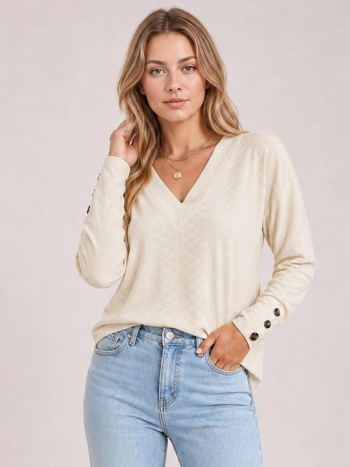Model poses in a cream V-neck long sleeve blouse with a relaxed regular-length silhouette, subtle solid texture, and button-detailed cuffs.