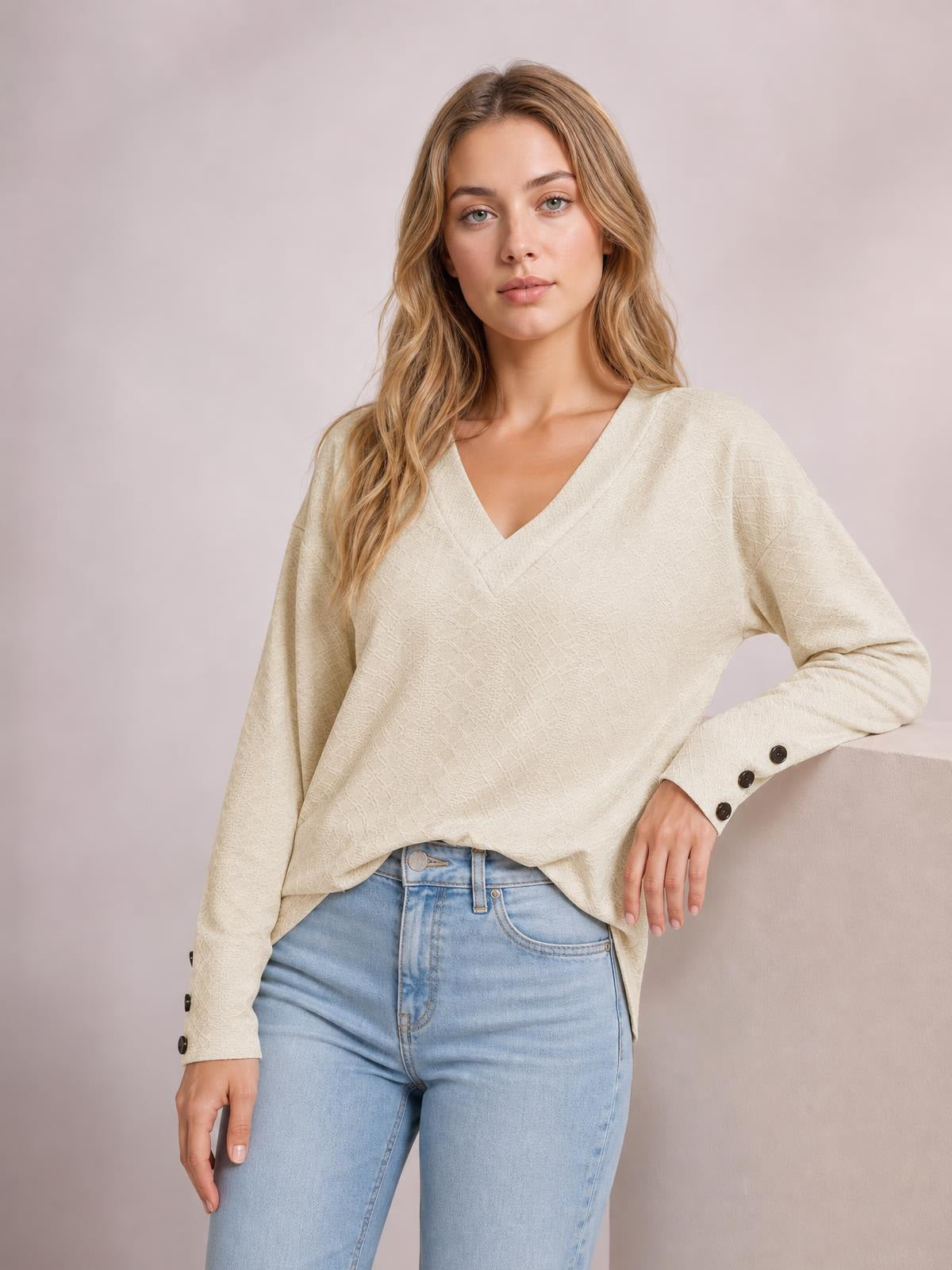 Model wearing a cream V-neck long sleeve blouse with a relaxed regular silhouette, textured fabric, and buttoned cuffs, posing with one hand on her hip.