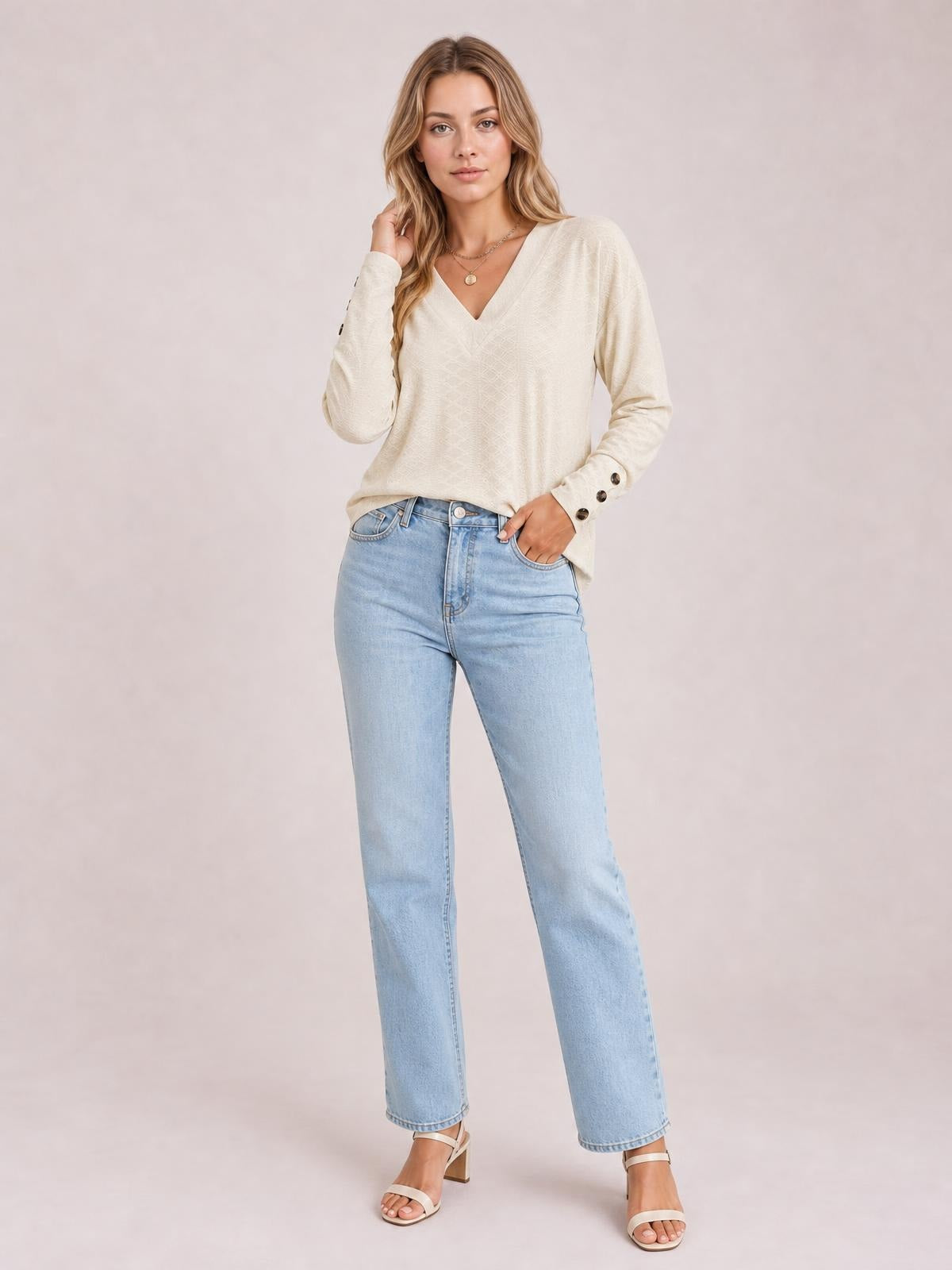 Model wears an ivory V-neck long sleeve blouse with a relaxed regular silhouette, opaque fabric, and buttoned cuffs, posing with one hand in her jeans pocket.
