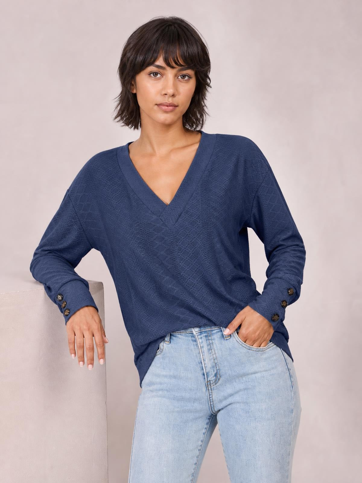 A model wears a navy blue V-neck long sleeve blouse with a relaxed regular silhouette, buttoned cuffs, and a slightly textured finish while posing with one hand in her pocket.