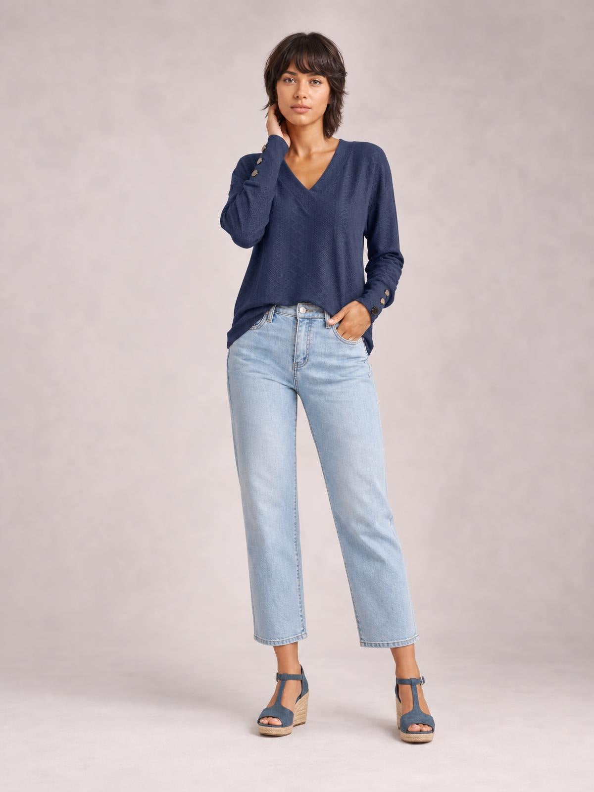 A model wears a navy blue V-neck long sleeve blouse with a relaxed regular-length silhouette and buttoned cuffs, posing with one hand at her neck.