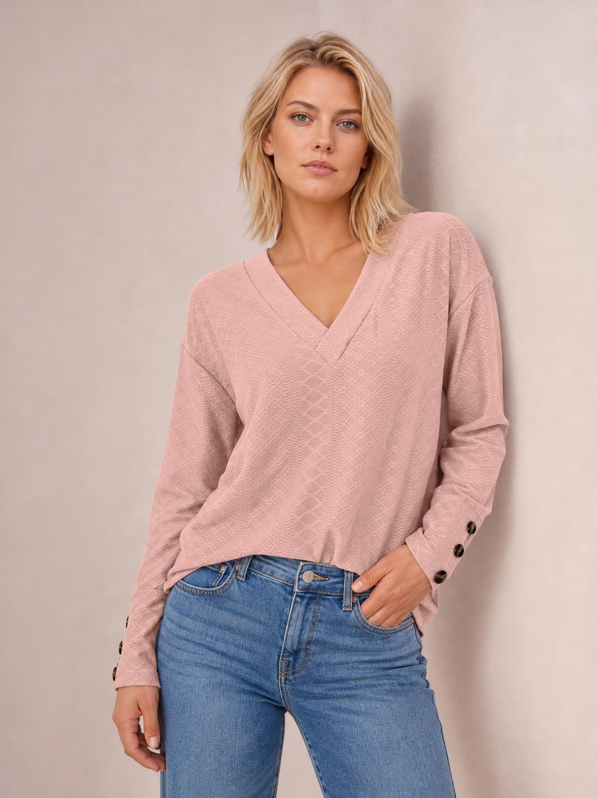 Model wears a blush pink V-neck long sleeve blouse with a relaxed regular silhouette, buttoned cuffs, and one hand tucked into her jeans pocket.