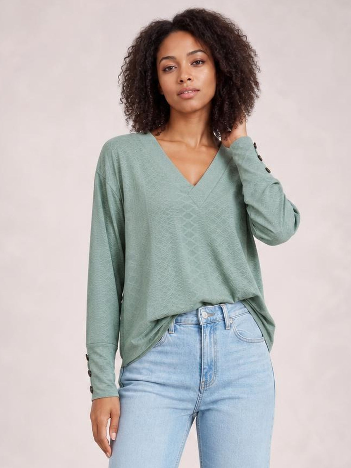 A model poses in a sage green V-neck long sleeve blouse with a relaxed regular silhouette and button-accented cuffs.
