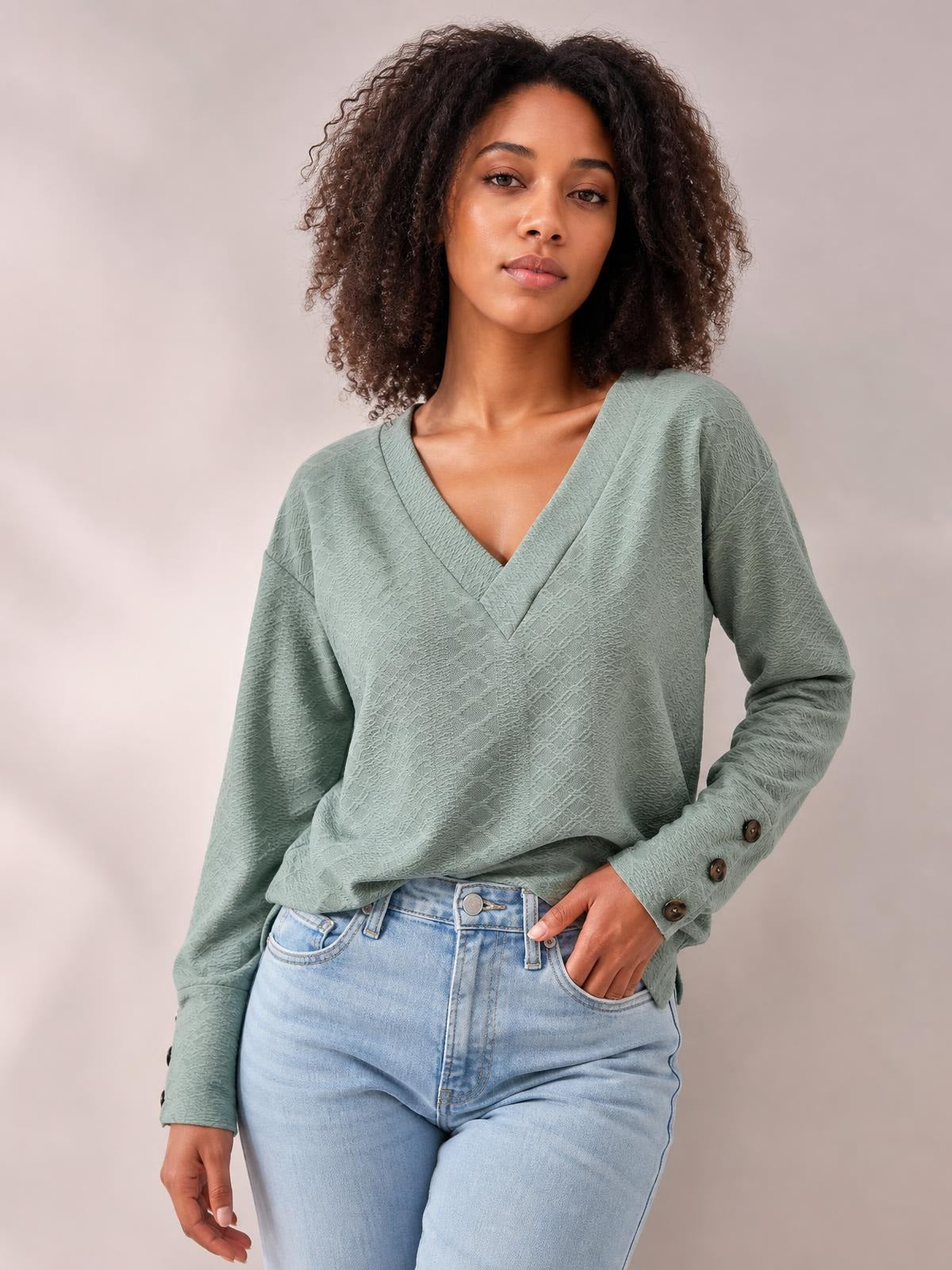 Model poses in a solid sage-green V-neck long sleeve blouse with a regular loose silhouette, textured fabric, and buttoned sleeve cuffs.