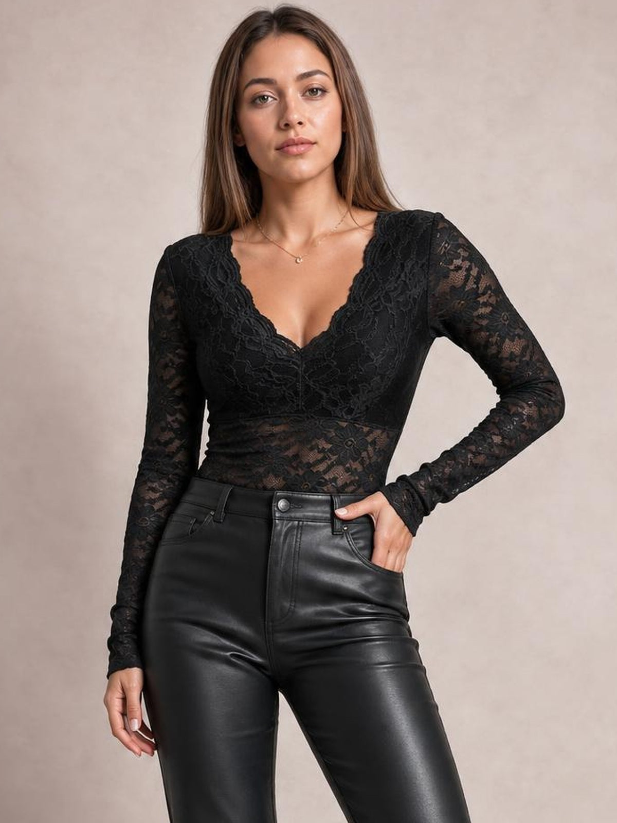 Model poses in a black V-neck long sleeve lace top with a fitted silhouette, sheer lace sleeves and bodice, and one hand in her pocket.