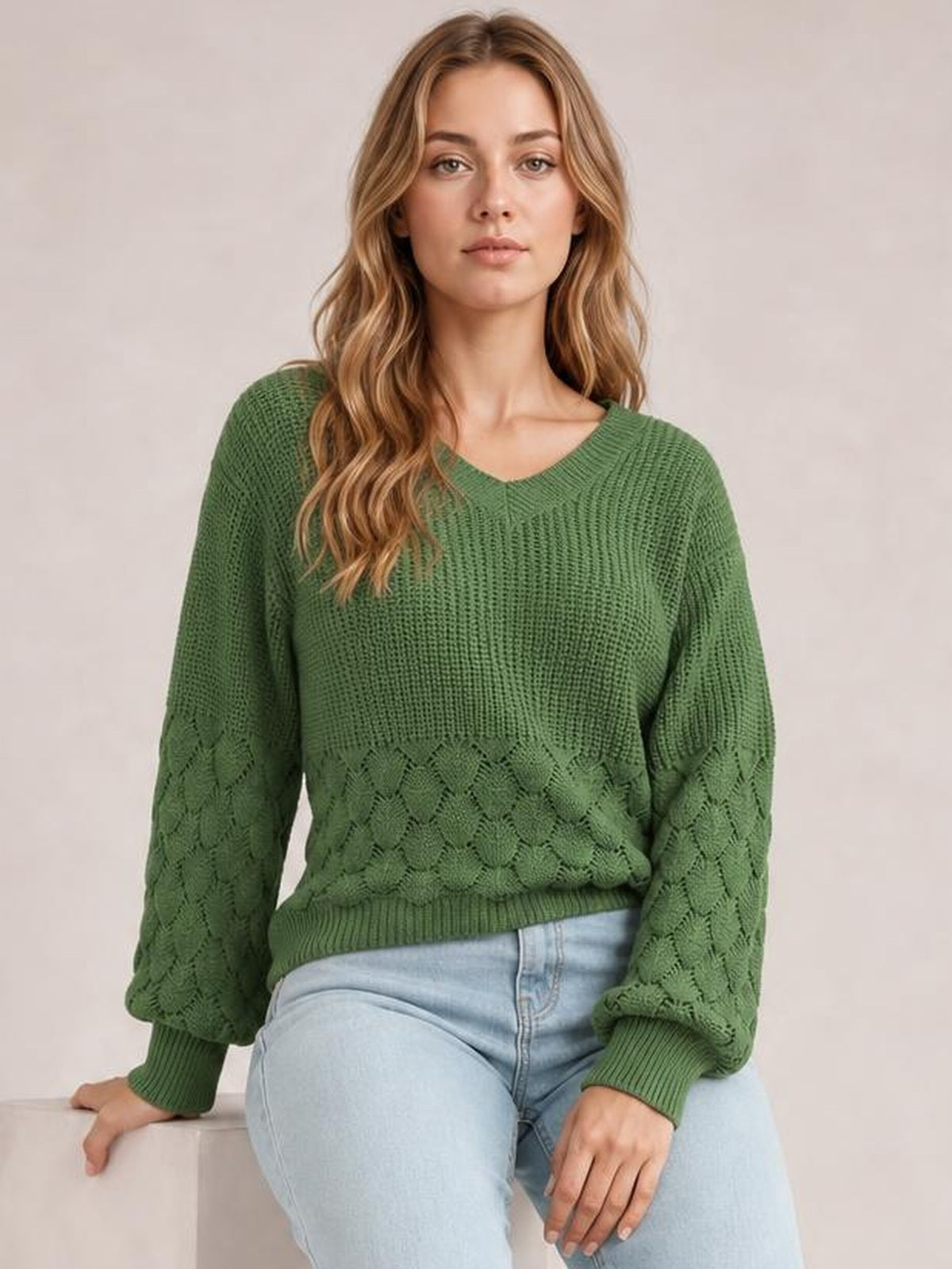 A model sits wearing a relaxed-fit green V-neck long sleeve sweater with textured knit panels, patterned sleeves, and ribbed cuffs and hem.