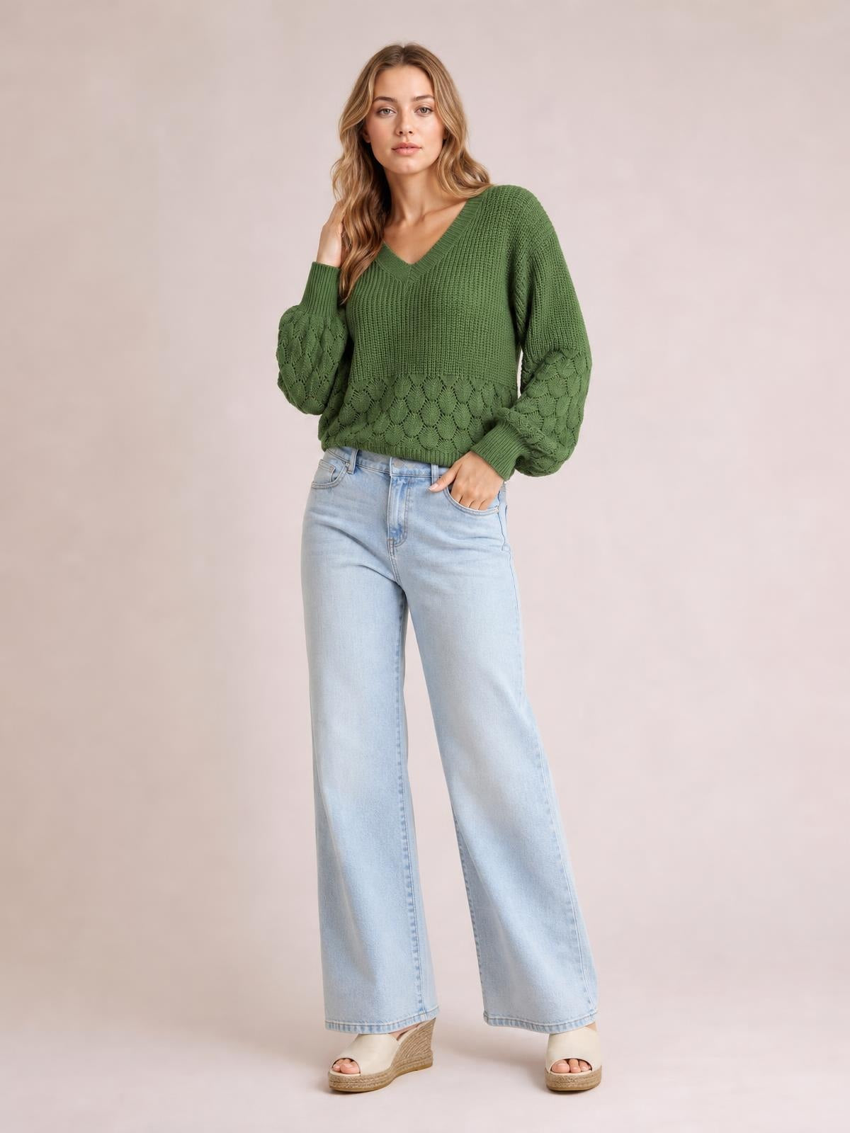 A model poses in a relaxed-fit olive green V-neck long sleeve sweater with ribbed trim, textured knit panels, and voluminous sleeves.