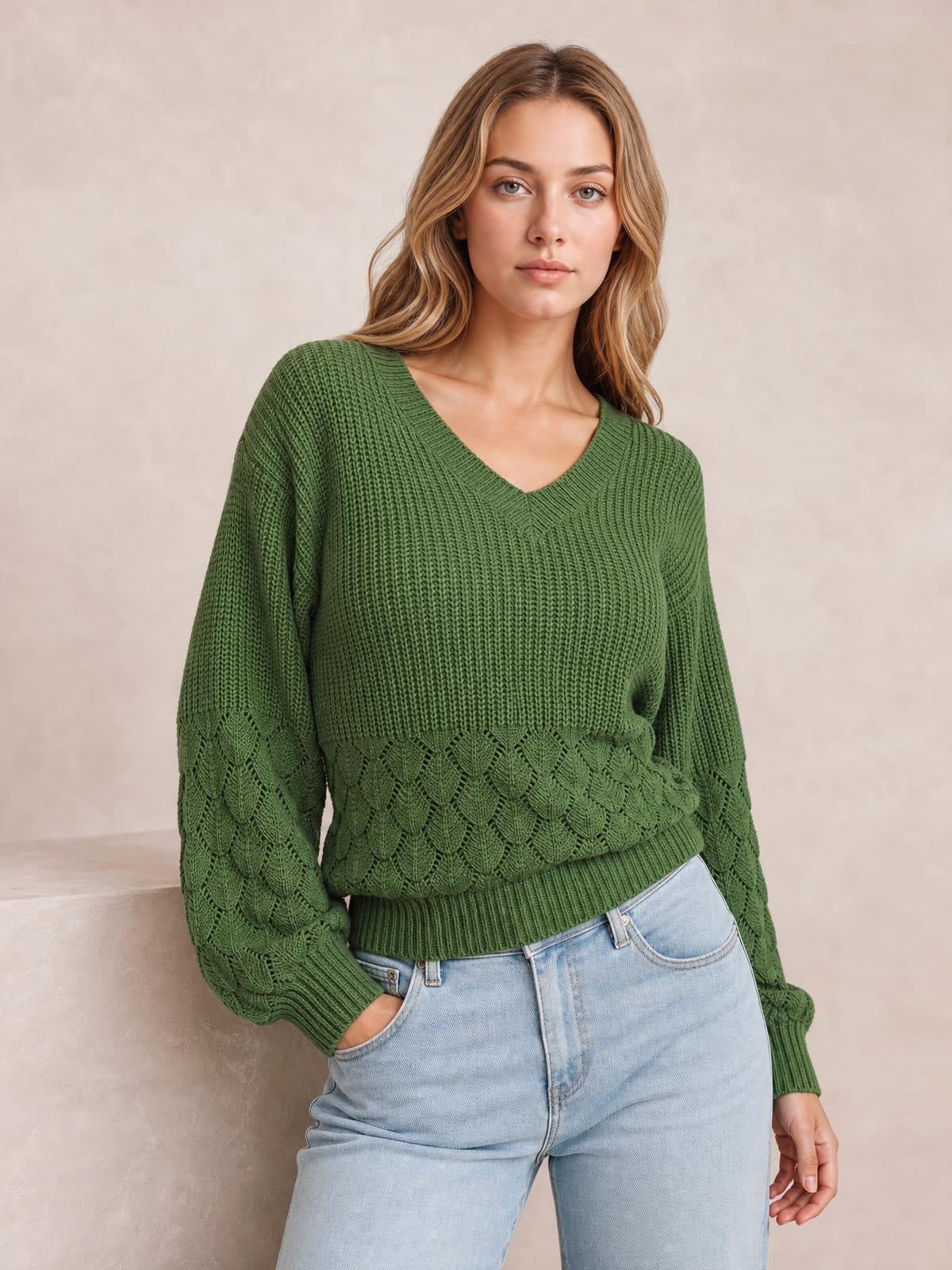 Model wearing a relaxed-fit green V-neck long sleeve sweater with textured knit construction, patterned sleeves, ribbed cuffs, and hem, posing with one hand in her jeans pocket.