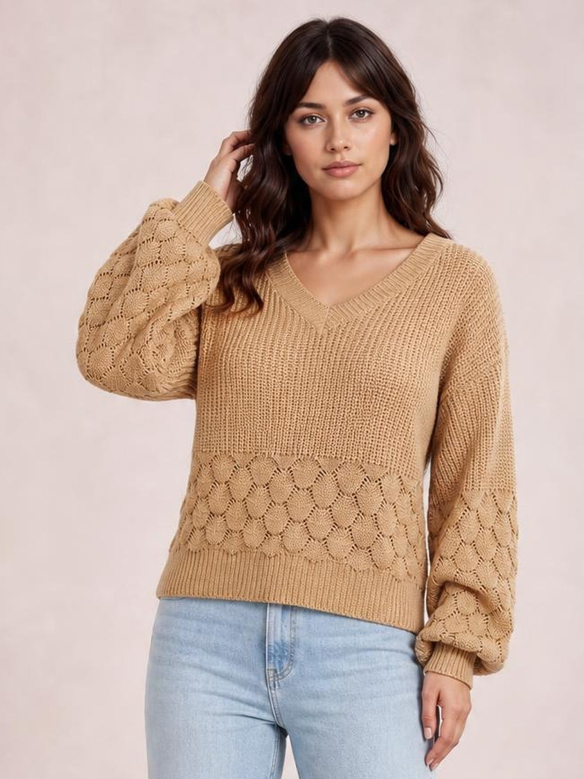 Model wearing a relaxed-fit camel V-neck long sleeve sweater with textured knit panels, ribbed cuffs and hem, posing with one hand in her hair.