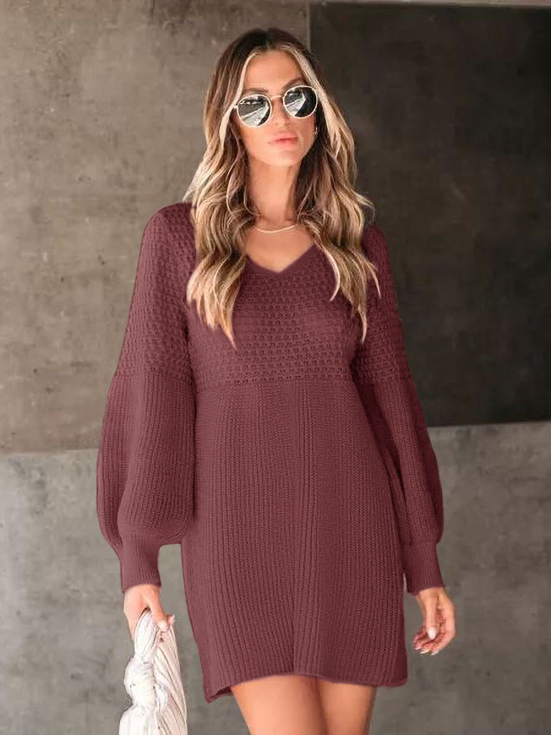 Model poses in a burgundy V-neck long sleeve sweater dress with a textured knit, relaxed above-knee silhouette, and gently gathered sleeves.