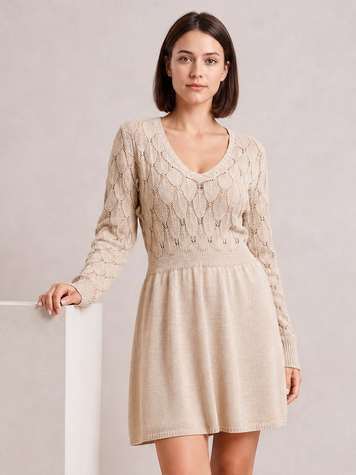 Model wears a beige V-neck long sleeve sweater dress with openwork knit detailing, a fitted waist, and a softly flared short silhouette.
