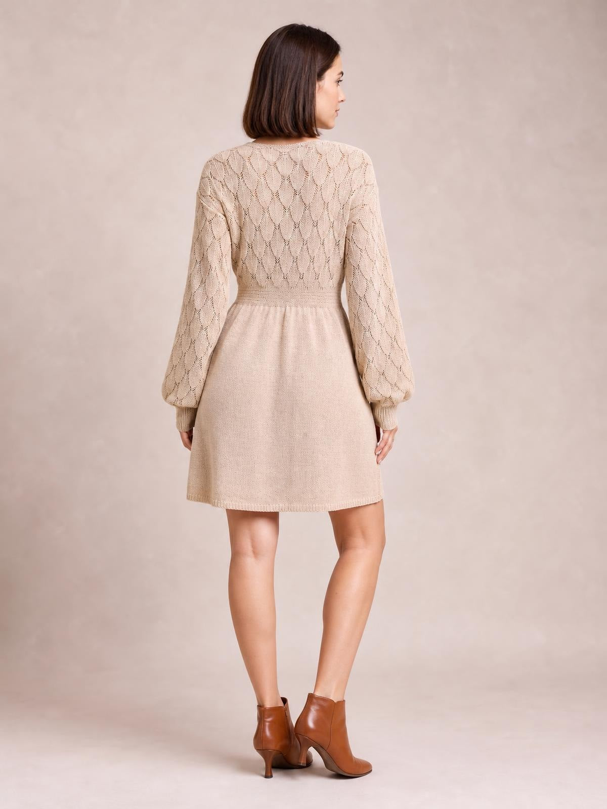 Model shown from behind wearing a cream openwork sweater dress with long sleeves, a fitted waist, ribbed cuffs, and a softly flared above-knee silhouette.