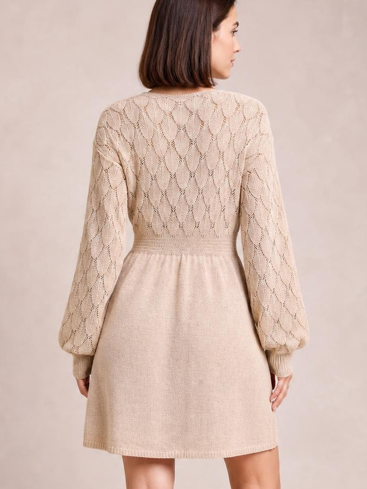 Model shown from behind wearing a cream long-sleeve sweater dress with openwork knit sleeves and bodice, fitted waist, flared silhouette, and ribbed cuffs and hem.