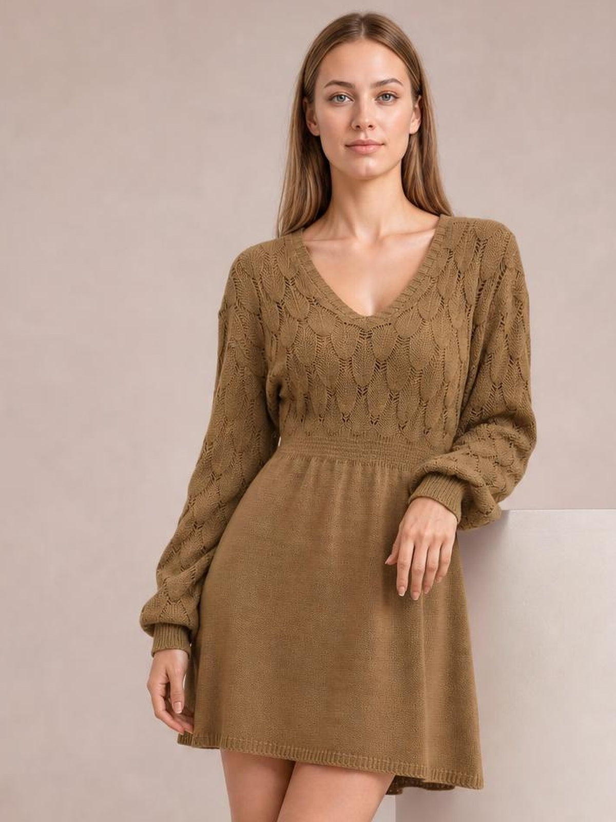A model wears a taupe V-neck long sleeve sweater dress with openwork knit detailing, a defined waist, and a softly flared mini silhouette.