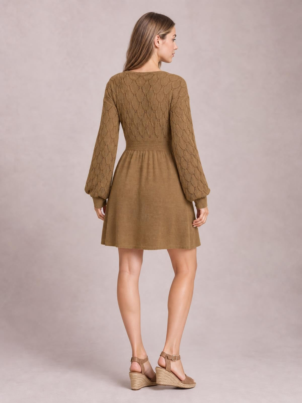 Model shown from behind wearing a camel-brown long-sleeve sweater dress with openwork knit sleeves and bodice, fitted waist, and flared above-knee skirt.