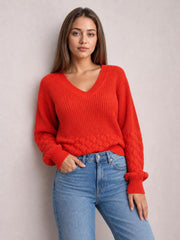 Model wears a bright red V-neck long sleeve sweater with a relaxed silhouette, ribbed trim, textured knit construction, and decorative openwork hem.