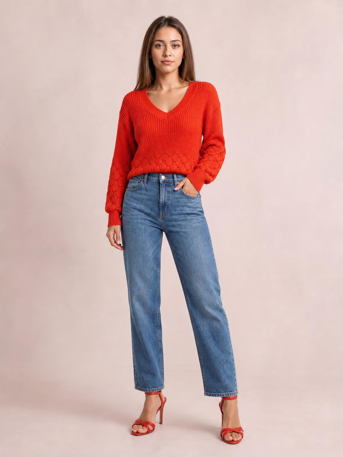 Model poses in a relaxed red V-neck long sleeve sweater with ribbed trim, textured knit details, and a comfortable silhouette styled with jeans.