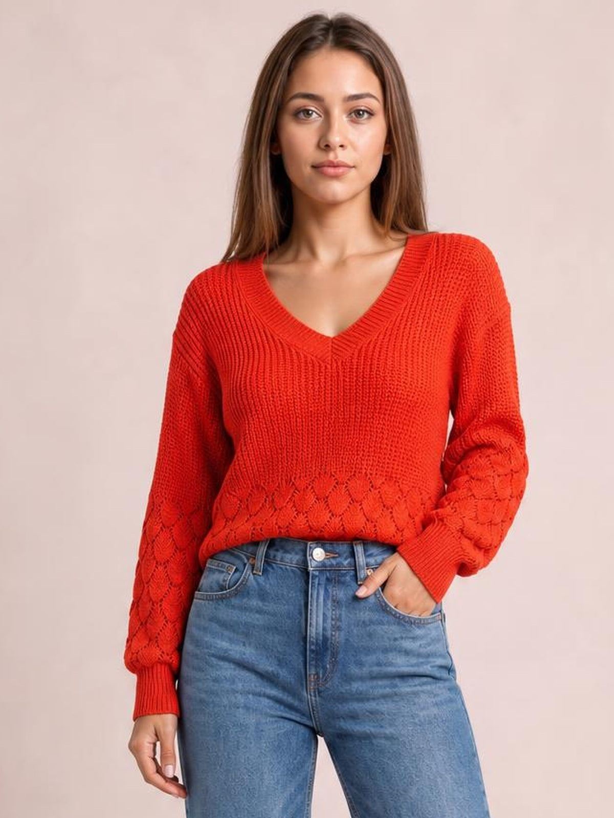 Model poses with one hand in her jeans pocket wearing a bright red V-neck long sleeve sweater with a relaxed silhouette, ribbed trim, and textured knit construction.