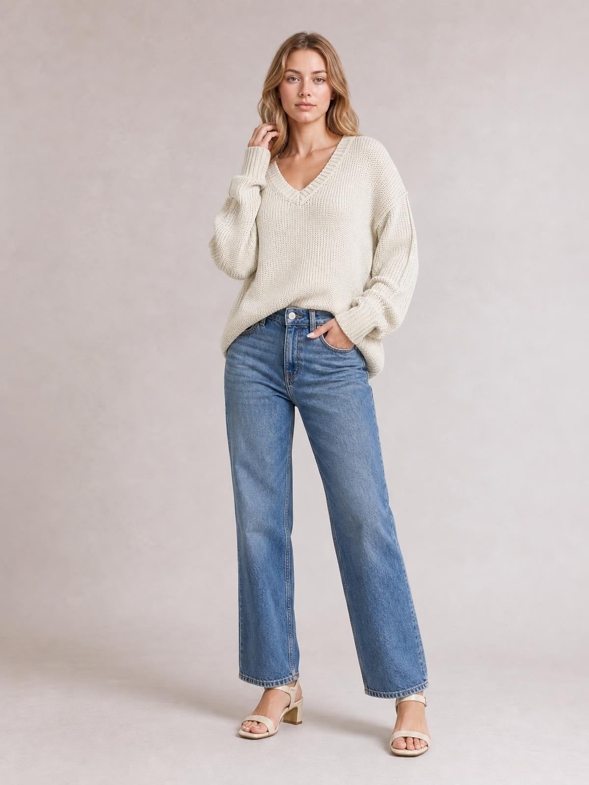 Model wears a cream V-neck loose knit drop shoulder sweater with ribbed trim, exposed seams, relaxed silhouette, and slightly oversized sleeves.