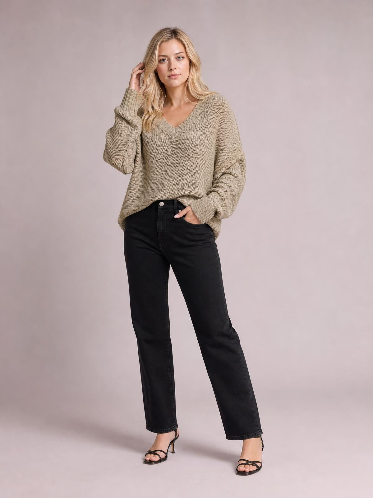 Model wearing a taupe V-neck loose knit sweater with drop shoulders, ribbed trim, exposed seams, and a relaxed oversized silhouette.