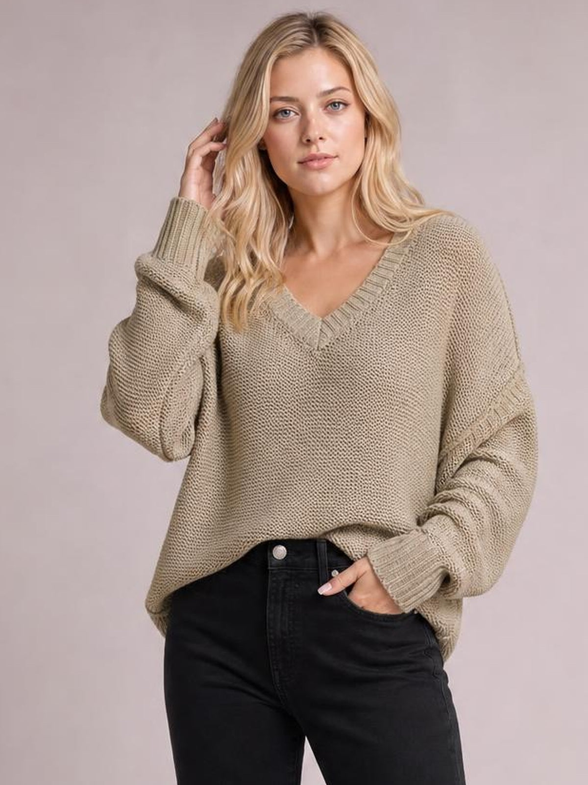 Model wearing a beige V-neck loose-knit sweater with drop shoulders, ribbed cuffs and neckline, exposed seams, and an oversized relaxed silhouette.