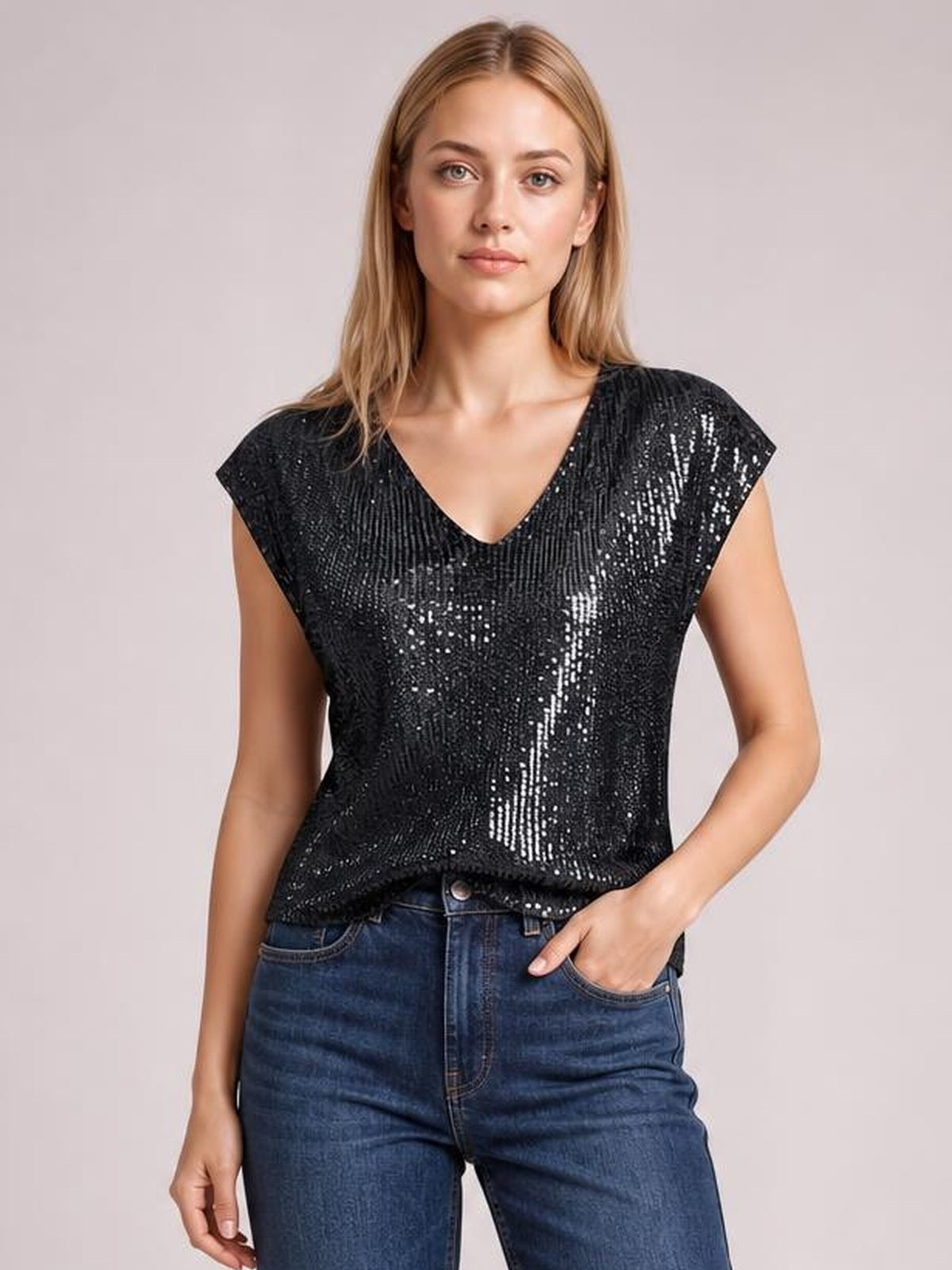 Model wearing a black V-neck sequin top with short cap sleeves and a relaxed, straight silhouette, paired with jeans and one hand in a pocket.