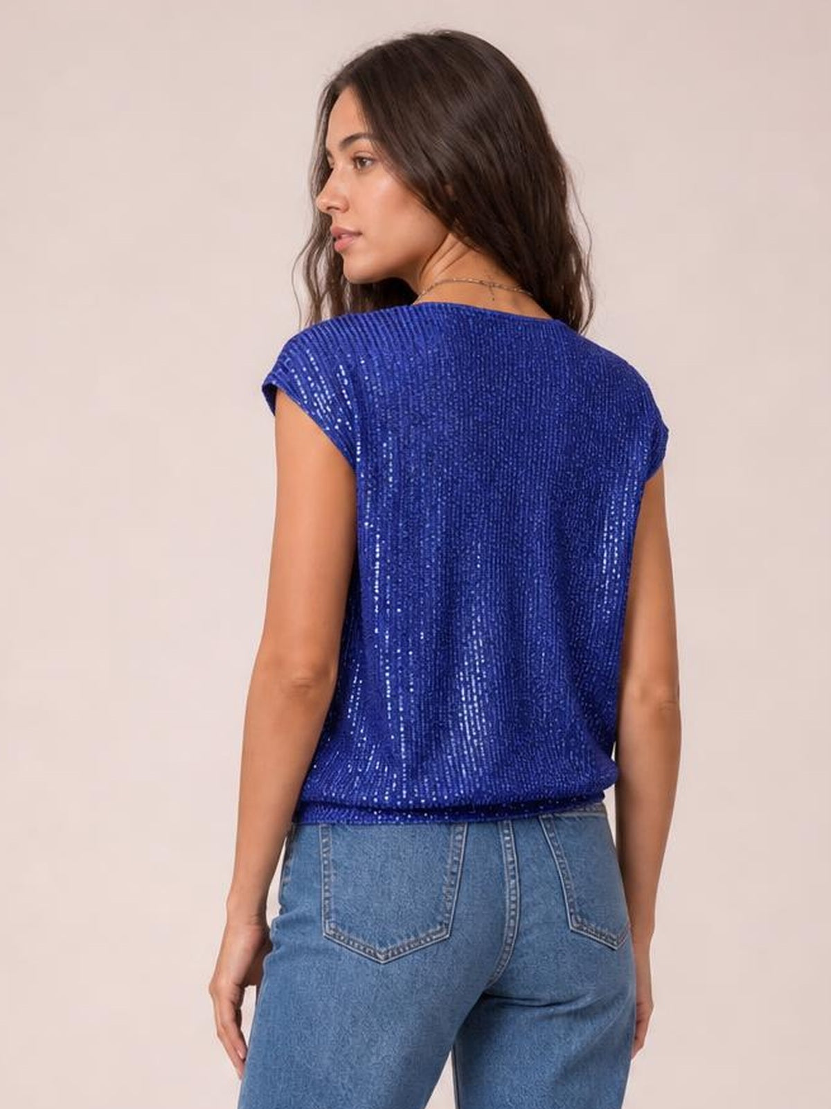 A model looks over her shoulder wearing a royal blue sequin cap sleeve top with a relaxed silhouette, shimmering texture, and straight hem.