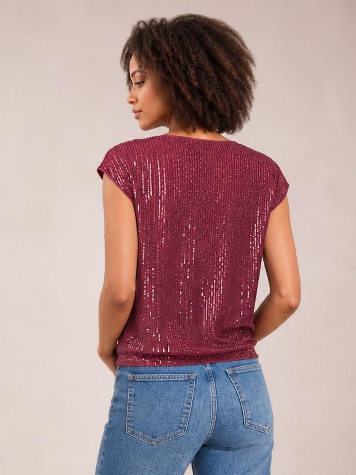 A model poses in a back view wearing a burgundy sequin top with short cap sleeves, a relaxed straight silhouette, and a slightly stretchy finish.