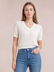 Model wears a white V-neck short sleeve knit top with a relaxed silhouette, textured front knit, ribbed cuffs and hem, and one hand in her jeans pocket.