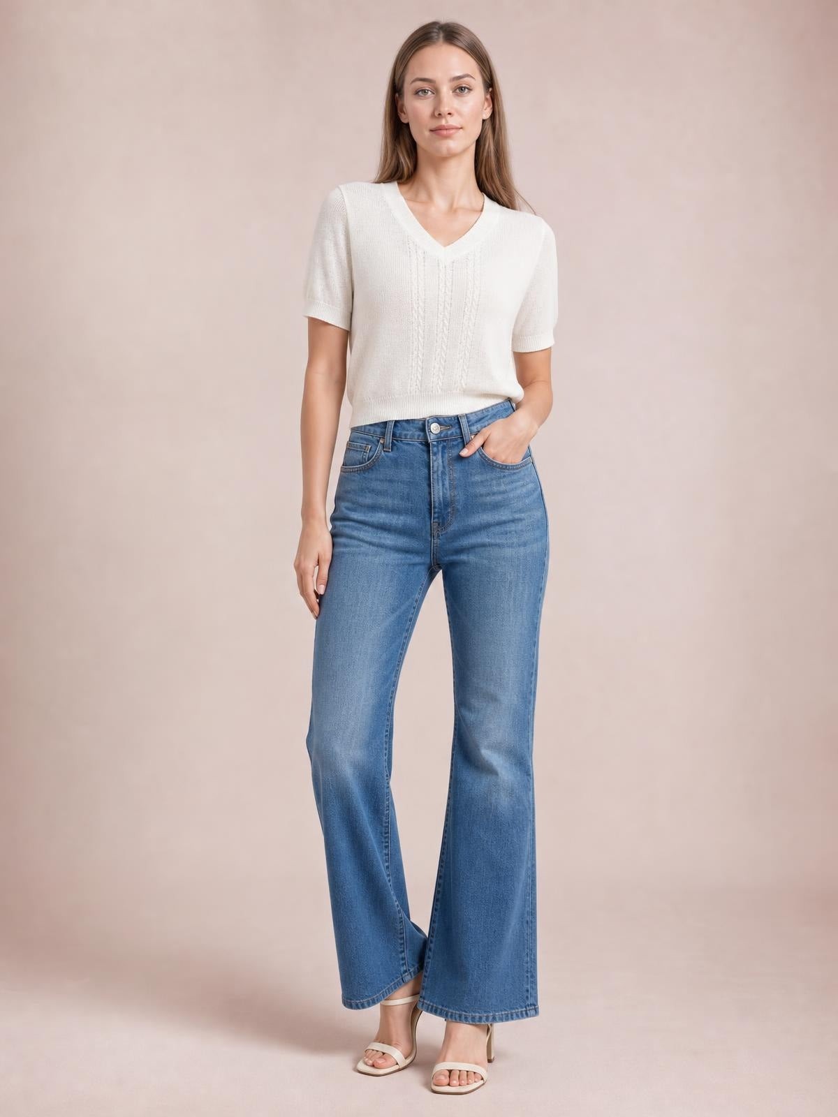 Model wears an ivory V-neck short sleeve knit top with a relaxed silhouette, ribbed trim, and subtle vertical textured stitching, posing with one hand in her jeans pocket.