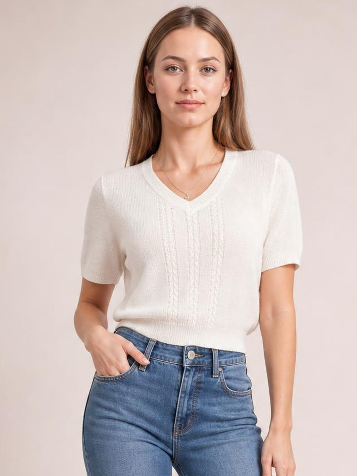 Model wearing a white V-neck short sleeve knit top with a ribbed hem, subtle cable-knit front detail, and relaxed silhouette, posing with one hand in her jeans pocket.